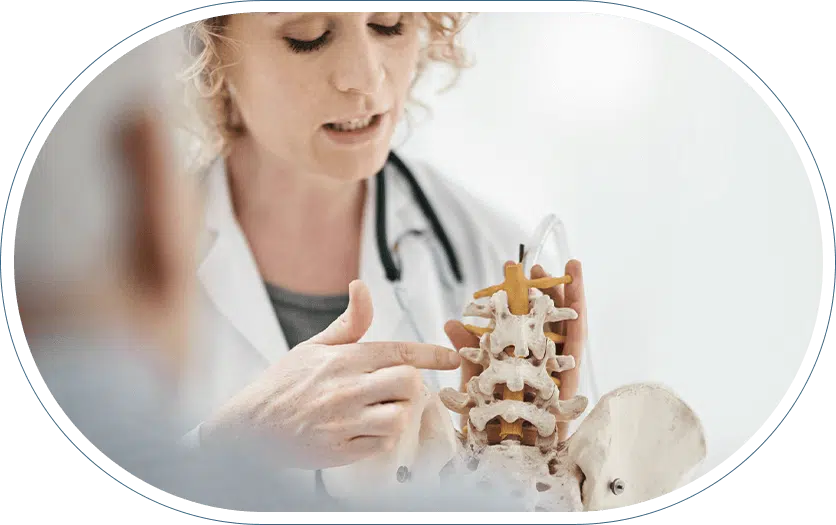 Female doctor explaining a spinal condition and osteoporosis treatment to her patient while using a model of a spine as a reference.